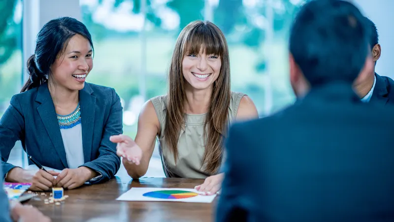 Three business people in a meeting discussing a pie chart on the table; two are women.