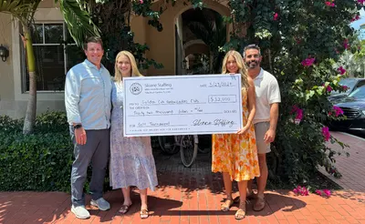 Four people hold a Sloane Staffing check for $32,000 payable to the Golden Cub Ambassadors Club for a golf tournament.