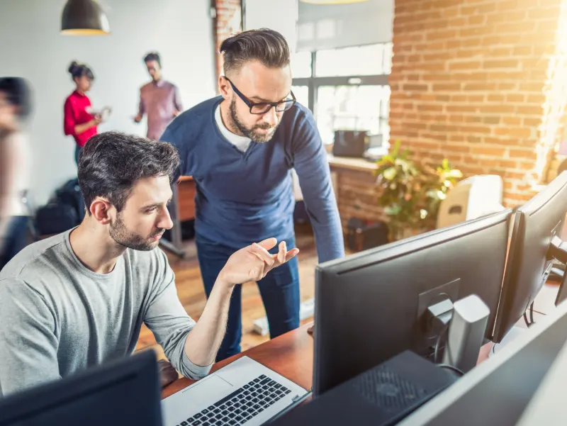 Two engineers collaborating at computer monitors in a modern office