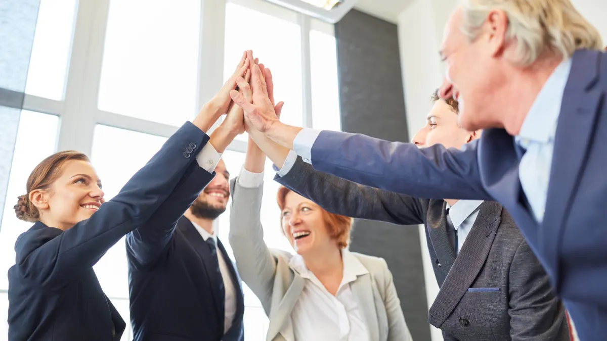 A group of diverse business people in suits high-fiving each other with smiles, celebrating.