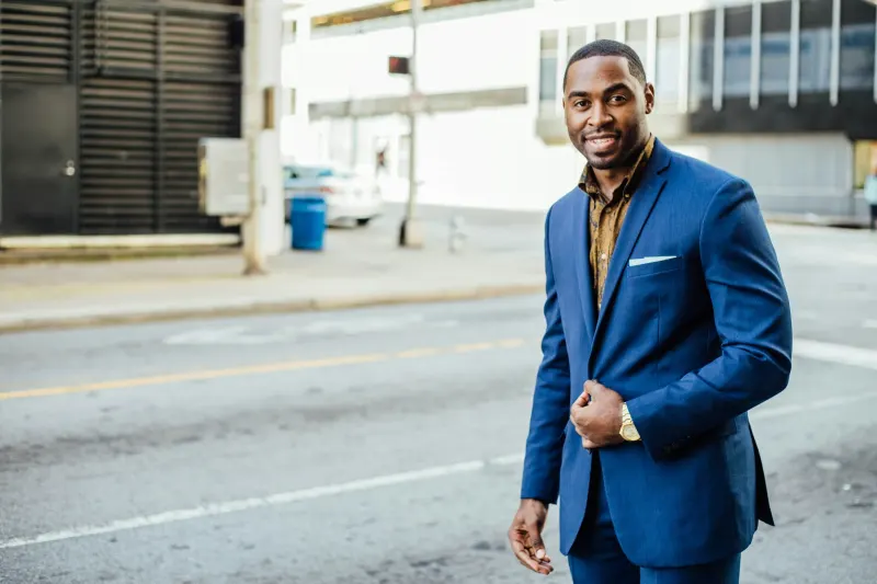 A man in a blue suit and patterned shirt smiles at the camera while standing on a city street — the investor-side view of portfolio hiring discussed in this post.