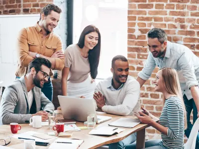 A diverse group of six professionals collaborating around a wooden table, all smiling and engaged in conversation.