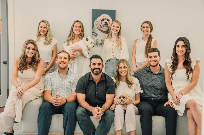 Team photo of 10 smiling people with two small dogs and a portrait of a dog in a spacesuit on the wall.