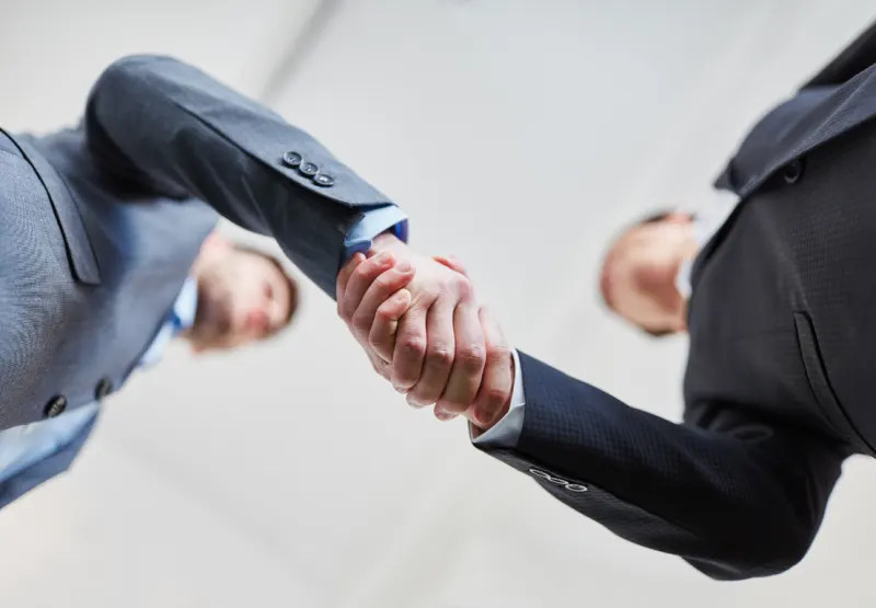 Two people in suits shaking hands, illustrating a customer success manager moving into an enterprise account executive seat