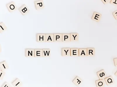 Scrabble tiles spell out “Happy New Year” on a white background with scattered tiles.