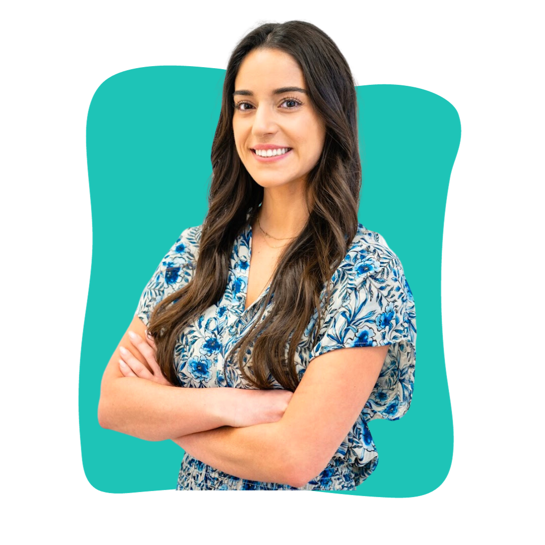 Smiling woman with long brown wavy hair wearing a blue floral print top, with her arms crossed.
