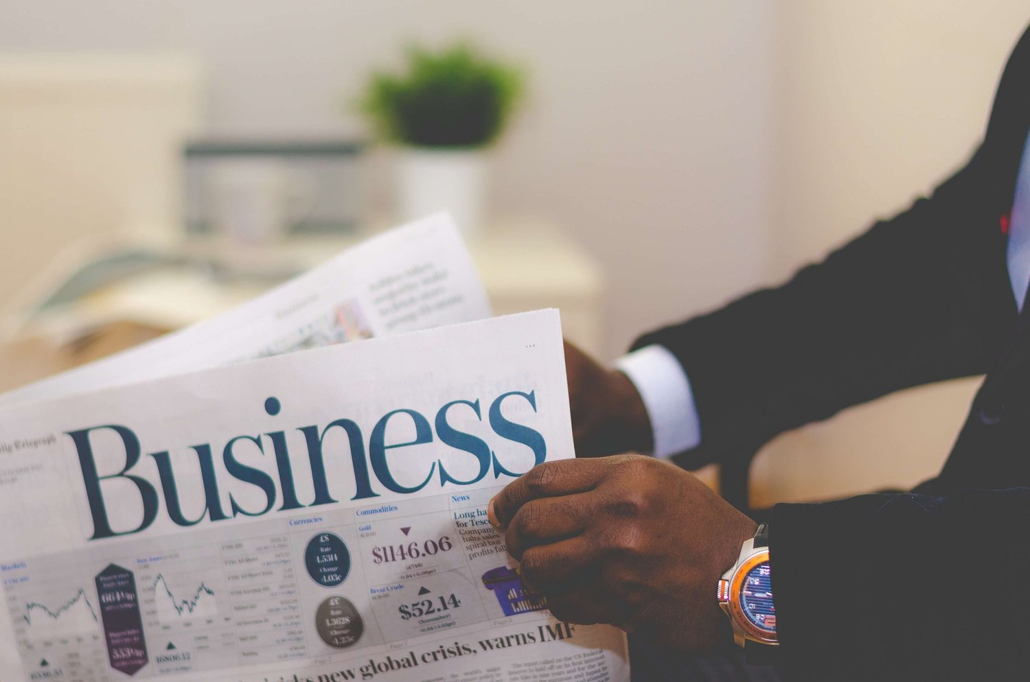 A person in a suit reads a newspaper with the headline “Business,” stock market charts visible.