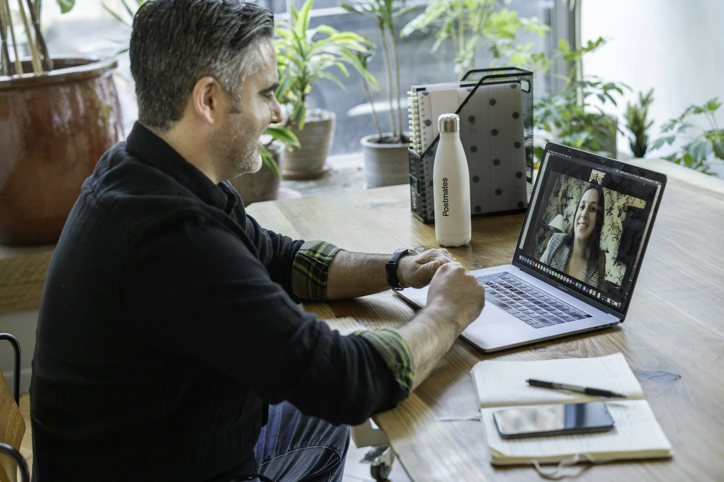 A man smiles while on a video call with a coworker on his laptop at a wooden desk.
