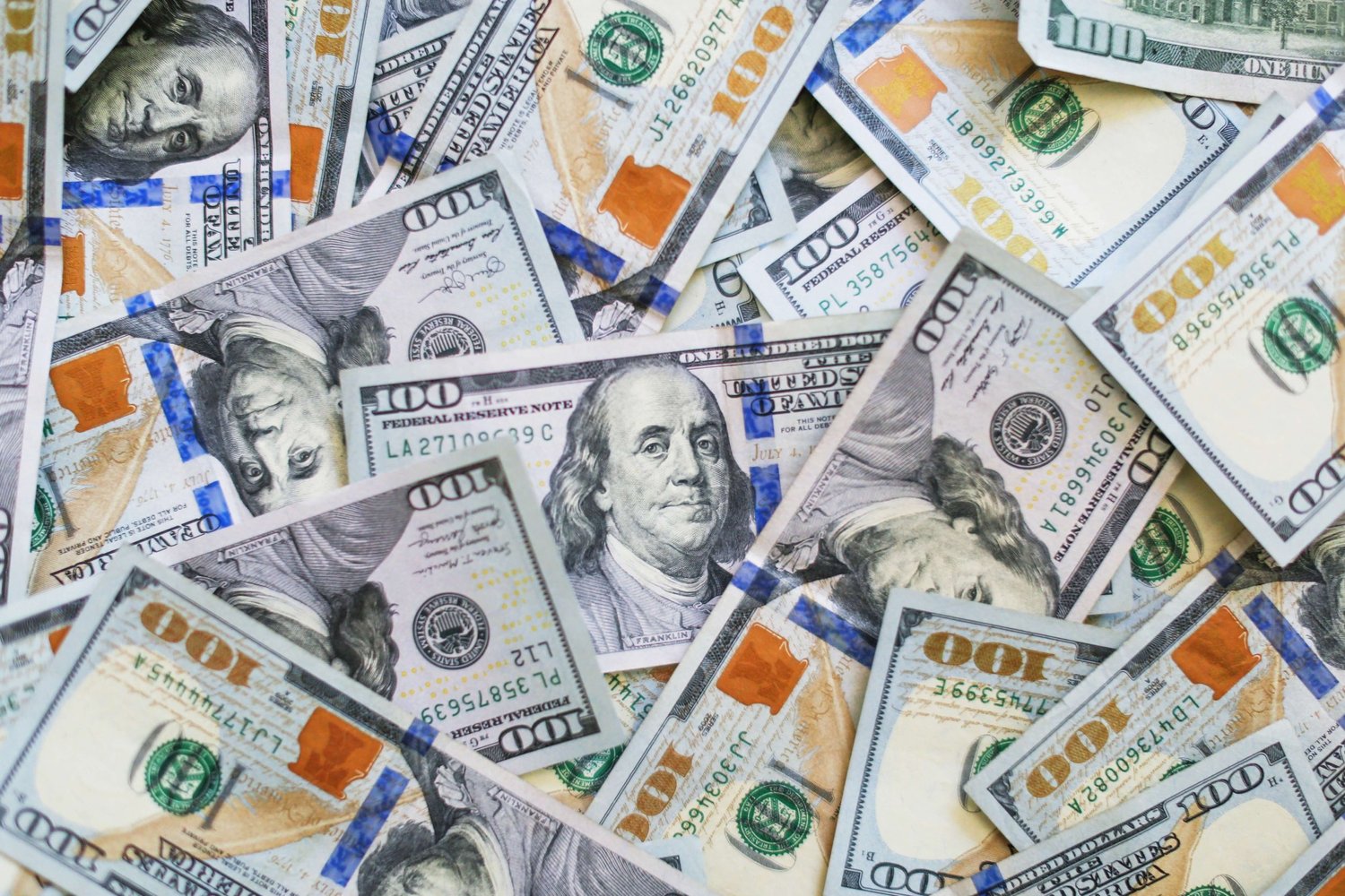 A dense pile of overlapping $100 bills featuring Benjamin Franklin, angled in various directions.