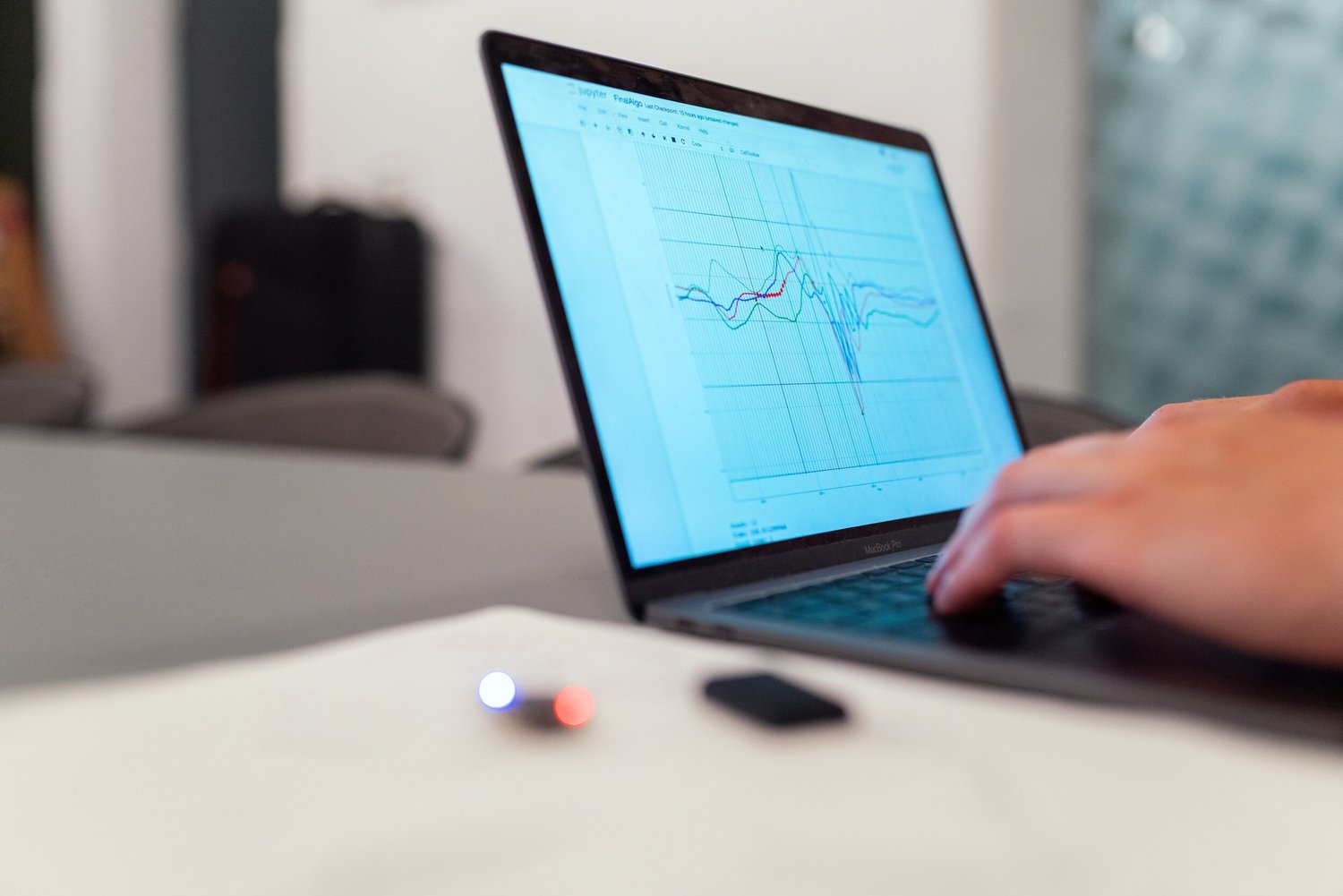 A person’s hand typing on a laptop displaying a line graph with multiple colored lines.