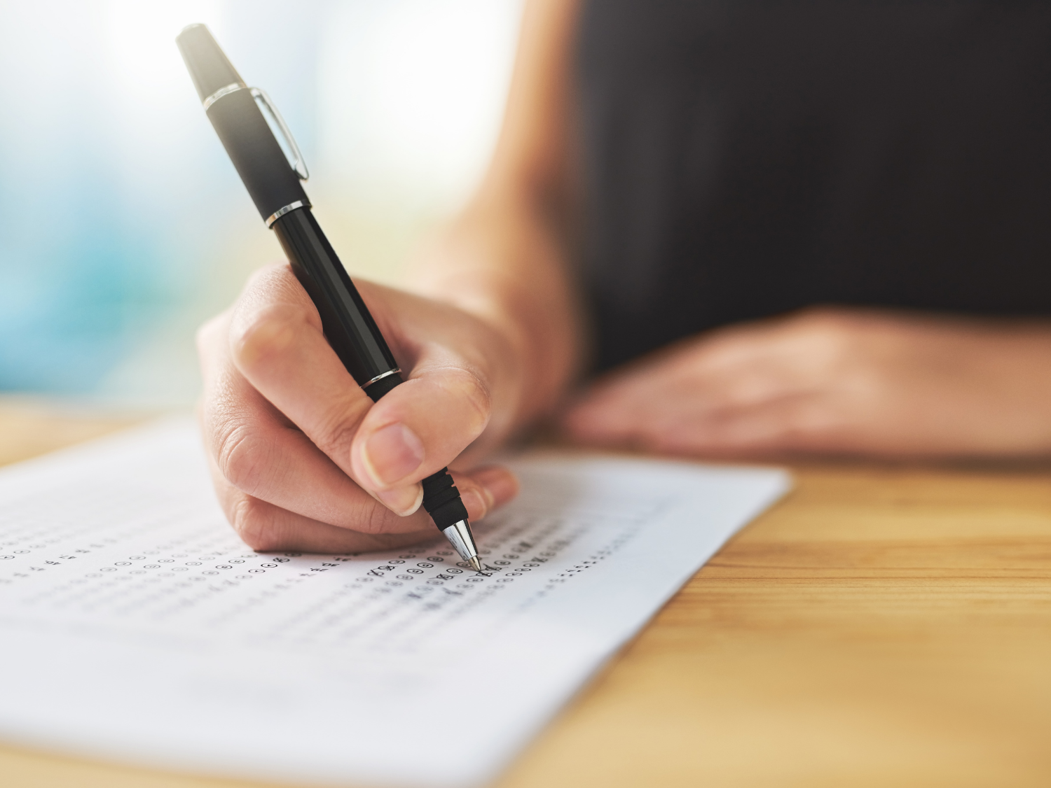 Close-up of a person’s hand filling out a bubble-sheet test with a pen.