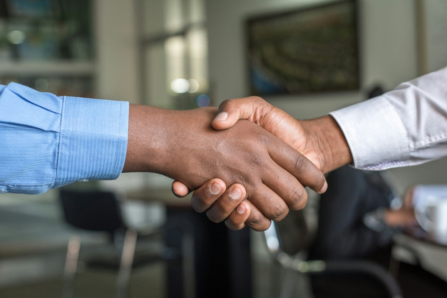 Two hands clasping in a handshake; one person wears a blue dress shirt, the other a white dress shirt.