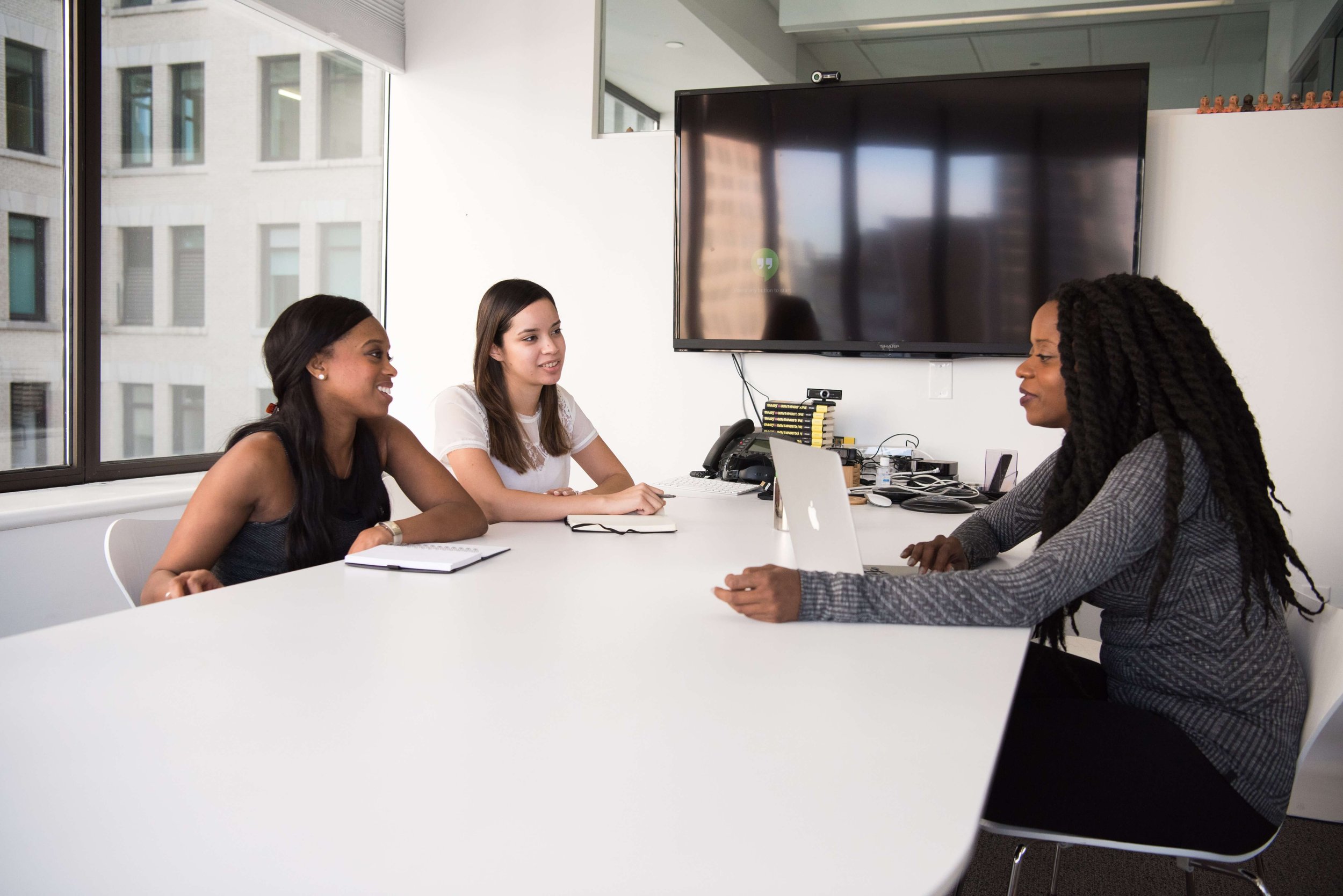 Three professionals in a bright meeting room, two interviewing a candidate seated across a white table