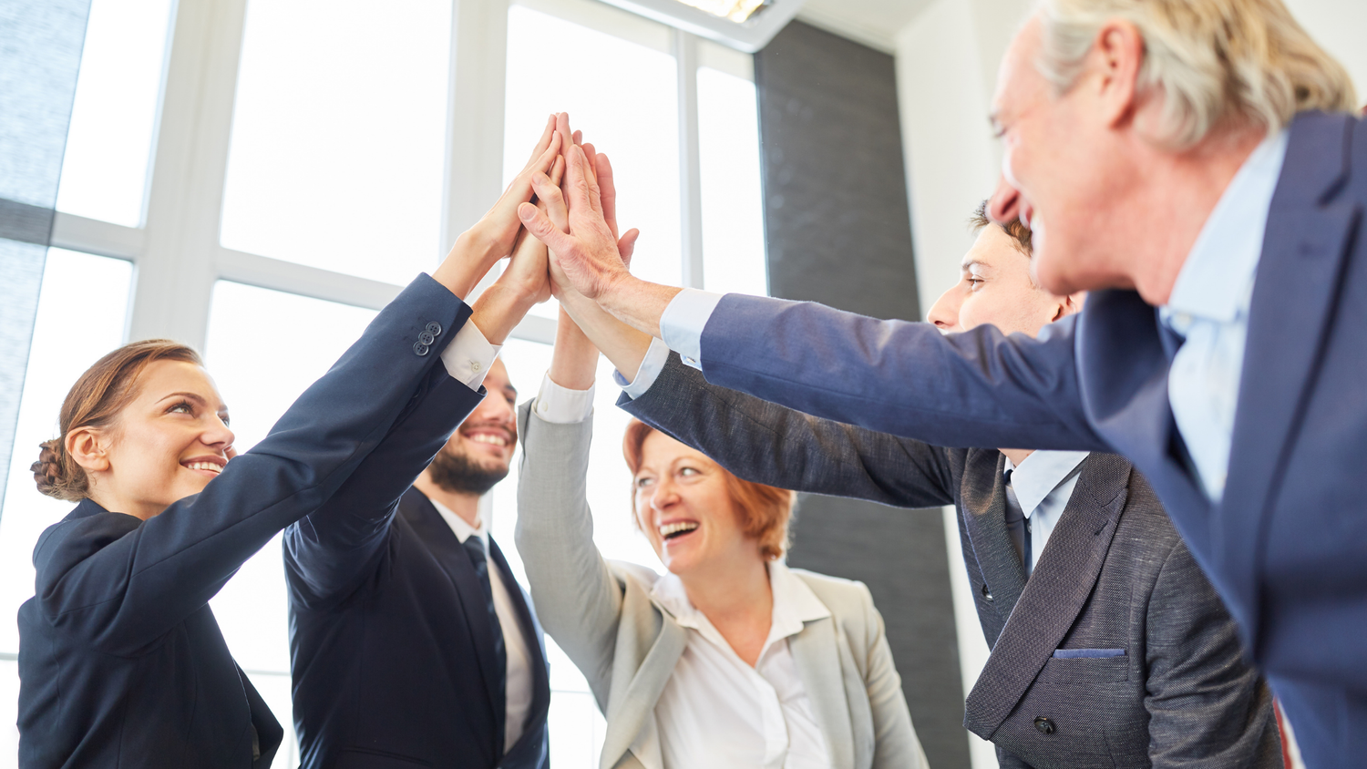 A group of diverse business people in suits high-fiving each other with smiles, celebrating.