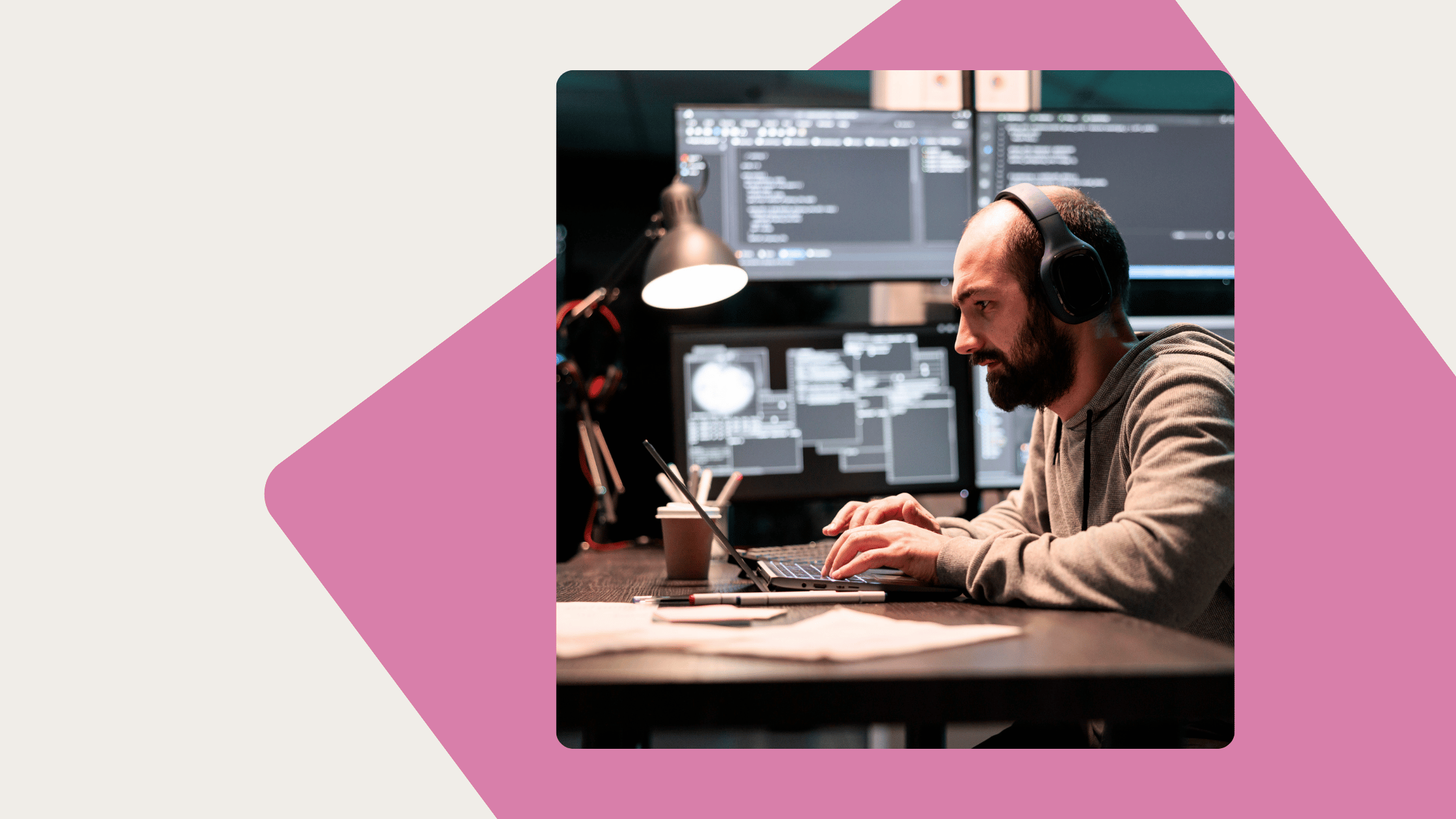 A man with headphones typing on a laptop in front of multiple computer monitors displaying code.