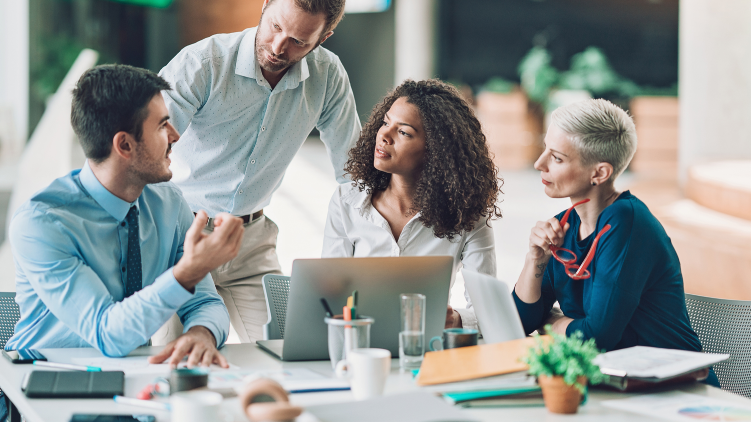 Four professionals in a meeting — two men and two women — discussing ideas around a table with laptops and papers.