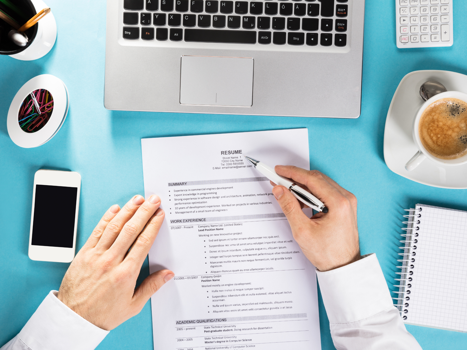 Overhead view of a desk with a resume, laptop, coffee cup, calculator, smartphone, and pen.