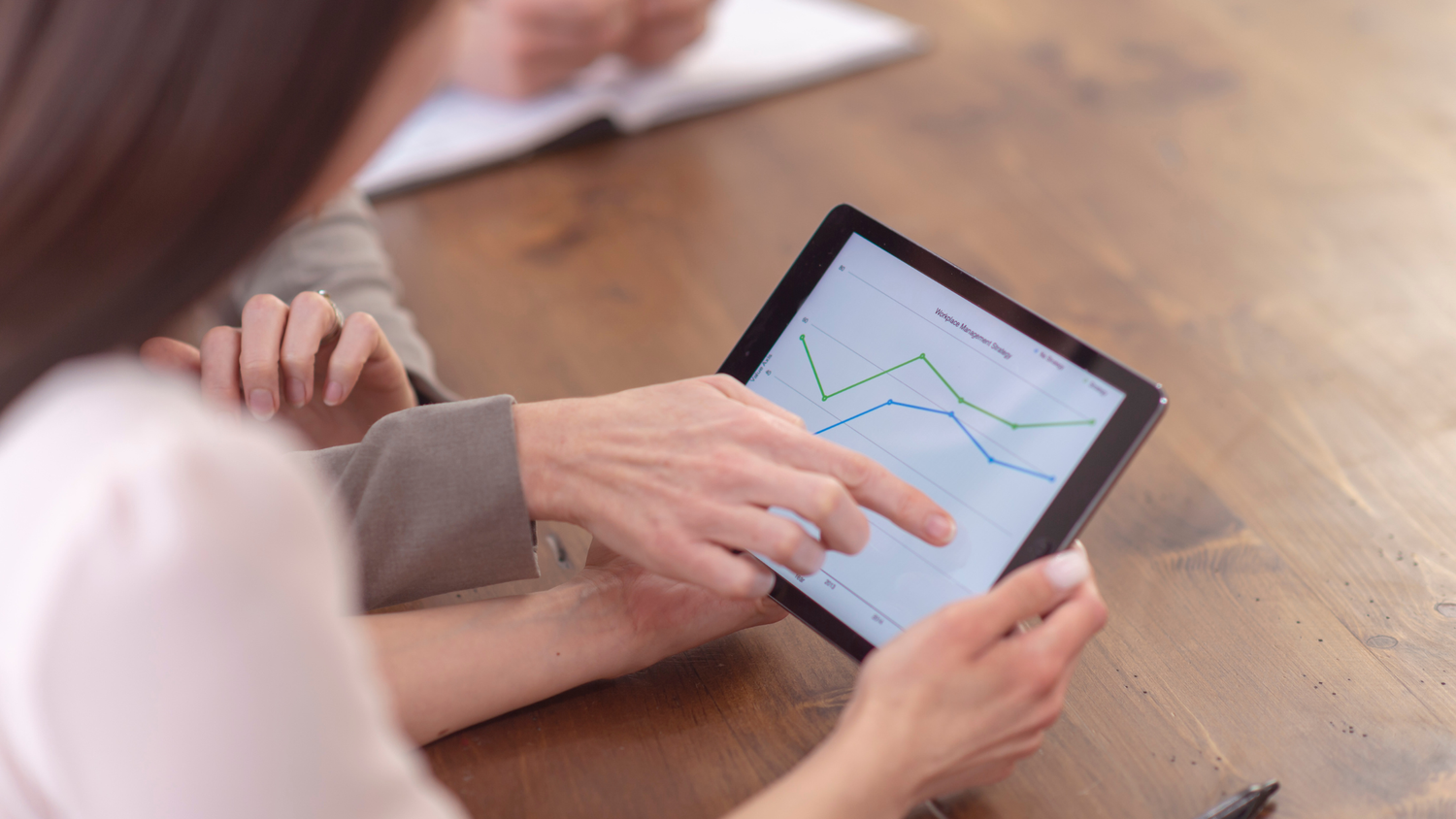 Two business people analyze a tablet displaying a Workplace Management Strategy chart with blue and green lines.