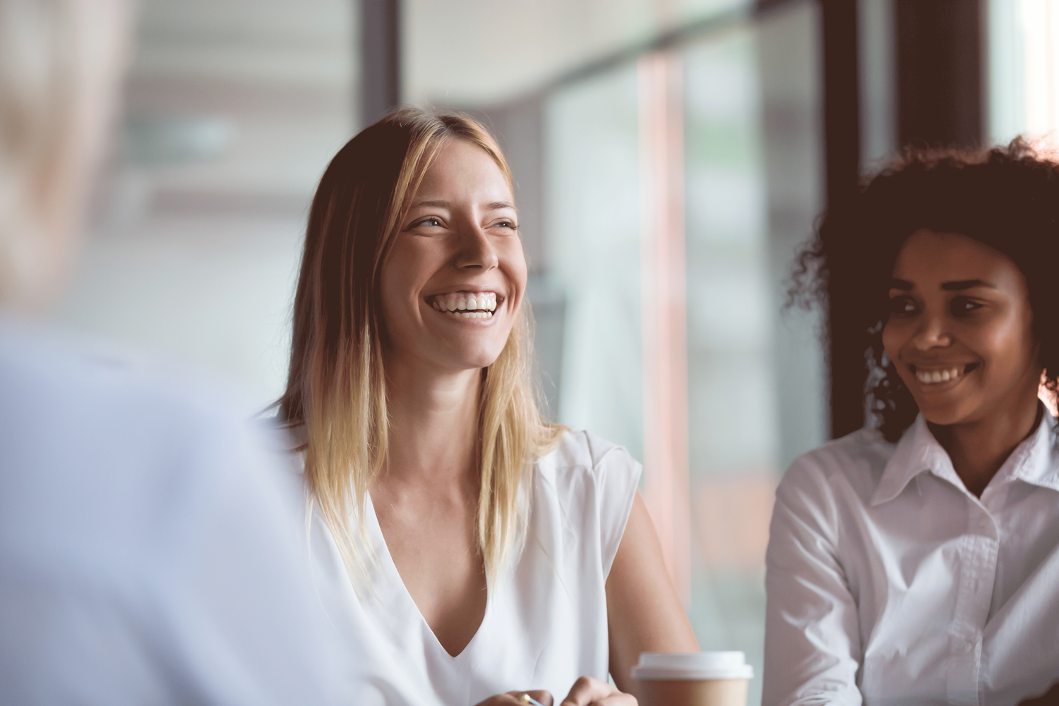 Two women in white shirts smiling during a meeting; the woman on the left laughs broadly.