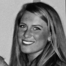 Black and white headshot of a smiling woman with long blonde hair wearing a dark jacket.