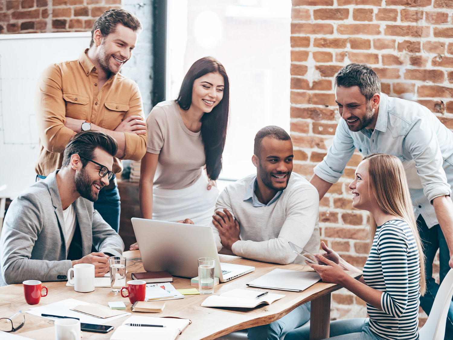 A diverse group of six professionals collaborating around a wooden table, all smiling and engaged in conversation.
