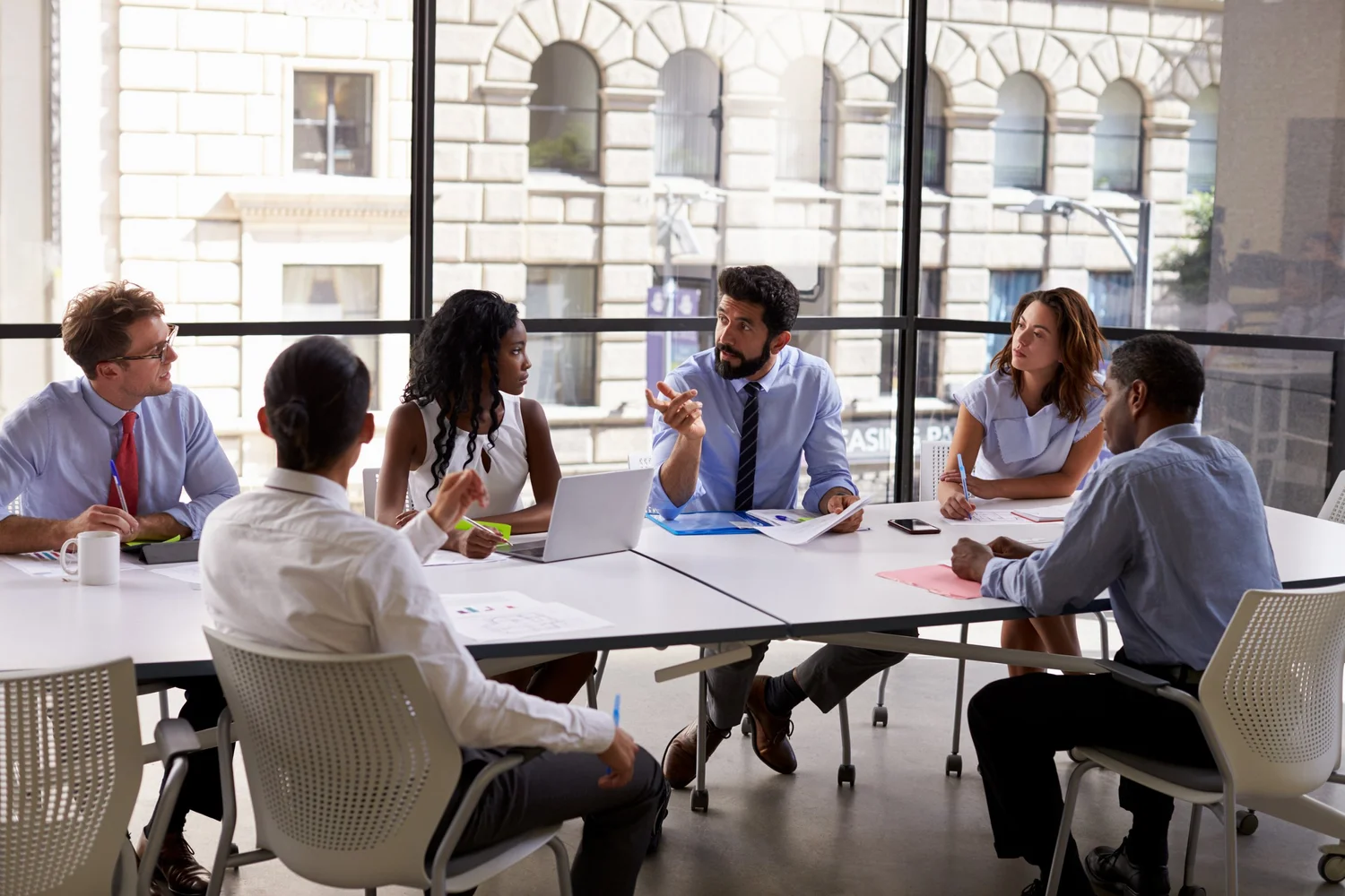 A diverse group of business professionals in a meeting discussing documents around a conference table.
