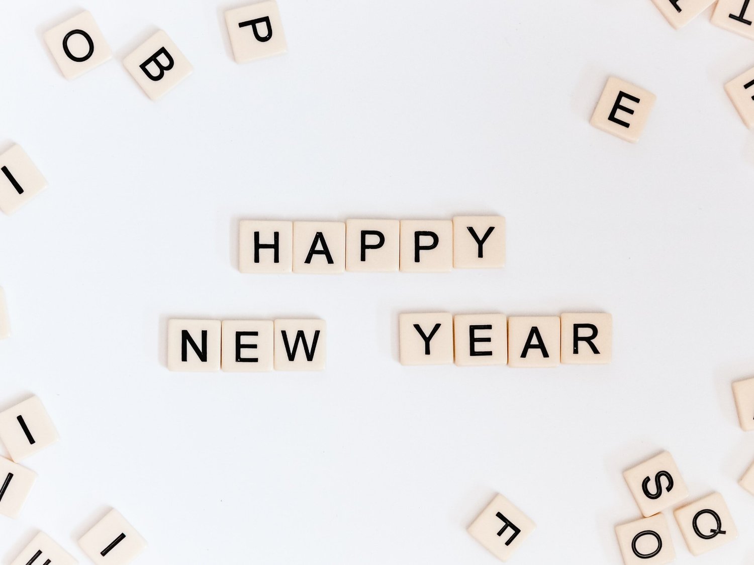 Scrabble tiles spell out “Happy New Year” on a white background with scattered tiles.