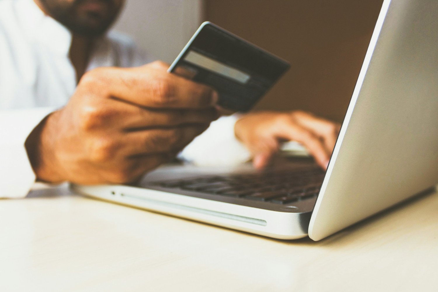 Person holding a credit card and typing on a laptop, likely online shopping or banking.