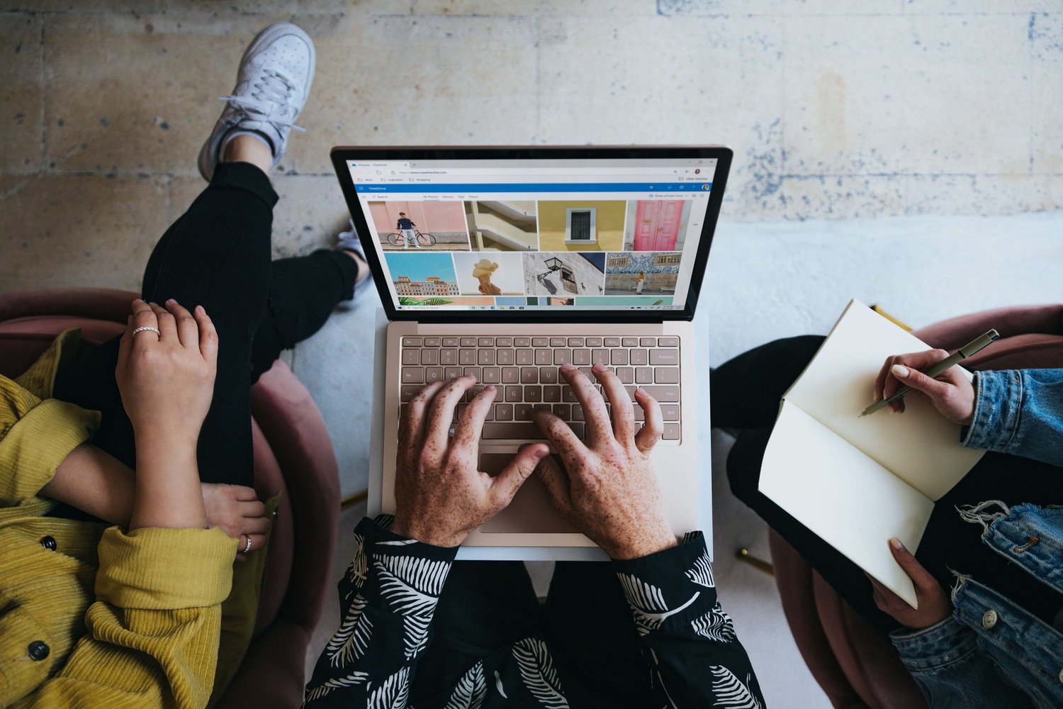 Overhead view of two people working on a laptop and notebook together; one types while the other writes.